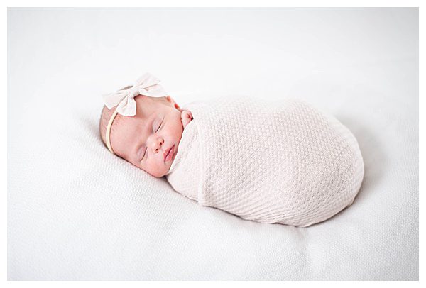 Swaddled newborn baby girl with bow