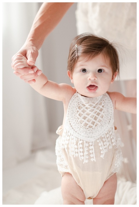 Mom holding 6 month old's hands helping to stand