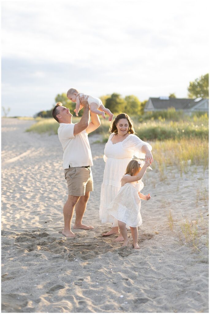 Happy family smiling, playing and dancing during a 6 month milestone family beach session in Westoport.