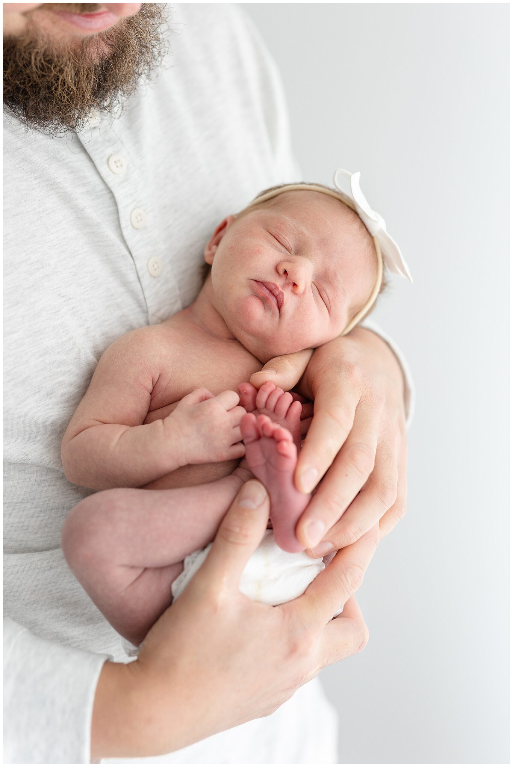 Baby girl curled up in dad's hands during sleepy newborn portraits