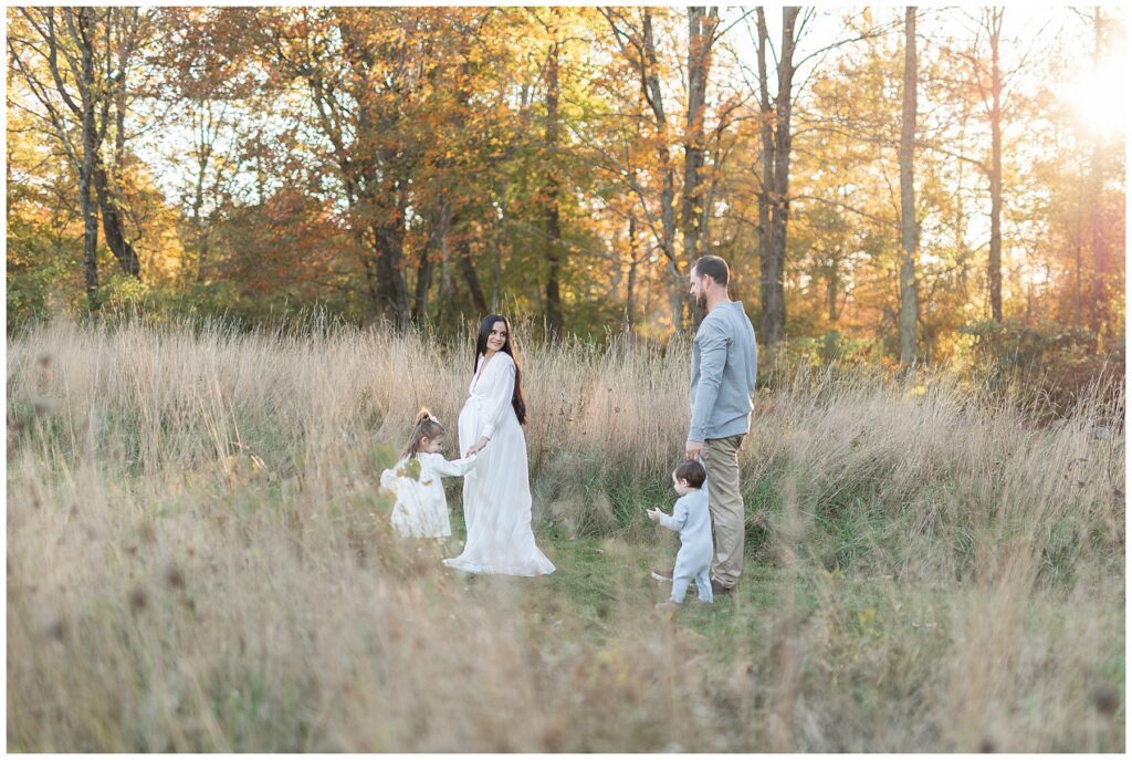Fall family maternity session in Newtown, CT with gorgeous fall foliage in background. Mom turns back and looks at dad.